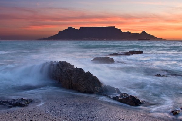 Снимка: DreamstimeTable Mountain – Южно Африканска РепубликаTable Mountain е планина с плосък връх, която представлява една от най-изтъкнатите забележителности, извисена над Кейптаун в Южна Африка, а изображението и е включено дори в официалния флаг на провинцията. Тази значима туристическа атракция привлича хиляди любопитни годишно, които биват качвани с помощта на голям лифт до приблизително 3 кв. километровото плато на върха и.Планината е обградена от Дяволският връх на изток и Лъвската глава на запад, които заедно са част от националния парк Table Mountain, а най-високата точка на тези възвишения достига 1086 м надморска височина. Тъй като името на планината се превежда като Планината Маса, заради плоскостта си, облаците, които често обвиват върховете ѝ, са станали популярни като Облачната покривка.